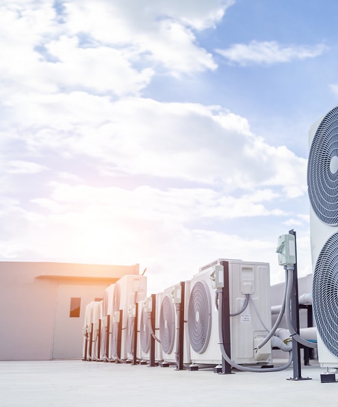 Série d'unités de climatisation (HVAC) sur un toit plat ensoleillé sous un ciel nuageux bleu.