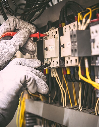 Mains gantées d'un technicien vérifiant des connexions électriques sur un panneau de contrôle avec un testeur.